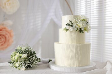 Delicious wedding cake with floral decor and bouquet on table indoors