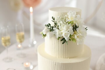Delicious wedding cake with floral decor on table indoors, closeup