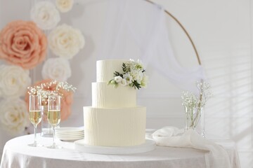Delicious wedding cake with floral decor and glasses of champagne on table indoors