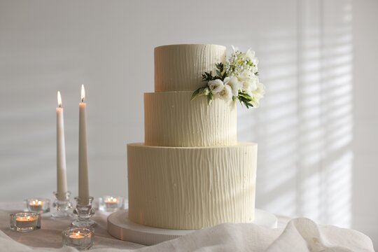 Delicious wedding cake with floral decor and burning candles on table indoors