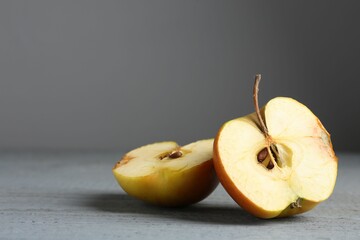 Halves of overripe apple on grey wooden table, closeup. Space for text