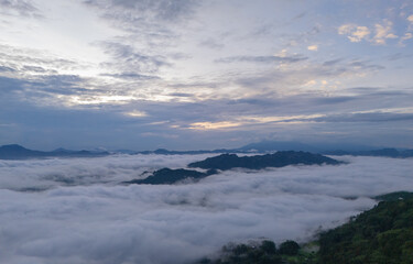 An wide Aerial view of a mountainous landscape with green fields and a village in the foreground. The mountain dominates the background, partially covered by clouds. Tana Toraja - Indonesia 