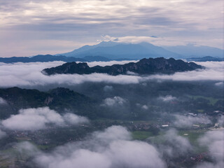 An wide Aerial view of a mountainous landscape with green fields and a village in the foreground. The mountain dominates the background, partially covered by clouds. Tana Toraja - Indonesia 