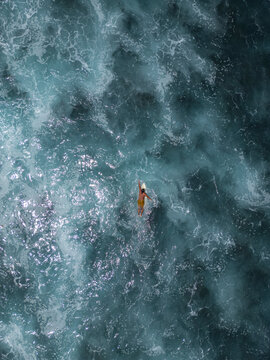 Aerial 90 degree straight down drone photo of a young male surfer on a surfboard in the white foamy ocean water. Pacific Coast, El Tunco beach town, El Salvador, Central America.	