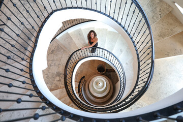 Beautiful woman looking up as she walks on an elegant spiral staircase made of marble. Luxury and elegance. 