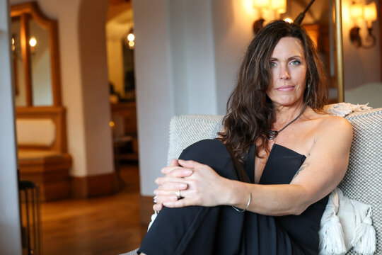Beautiful woman dressed elegantly in a black pant suit or jumper. Her fingers are interlaced and she has a friendly expression on her face. 