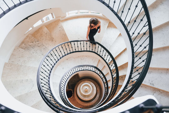 Attractive middle aged caucasian woman wearing a black jump suit in an elegant setting. She is walking down a spiral staircase made of marble. Luxury lifestyle, 