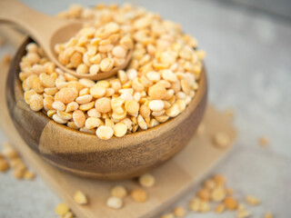 A pile of dried yellow split peas in a wooden bowl on a concrete background