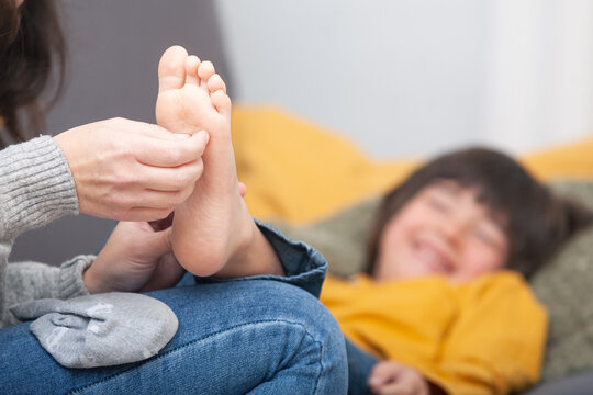 Close-up of mother&rsquo;s hands tickling her son&rsquo;s bare foot &ndash; joyful child in background