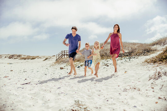 Young family walking on a sandy beach next to the ocean - Powered by Adobe