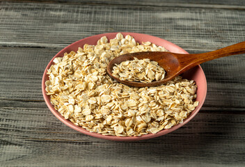 A bowl filled with rolled oats sits on a rustic wooden surface. A wooden spoon rests partially in the oats, suggesting readiness for cooking or preparing a wholesome breakfast