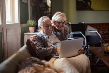 Elderly couple embracing while using laptop at home