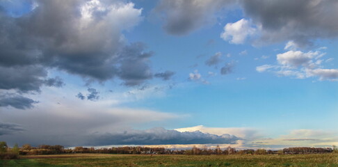 Expansive landscape showcasing a dramatic sky filled with clouds and blue hues over a serene field, illustrating the beauty of nature and tranquility concept