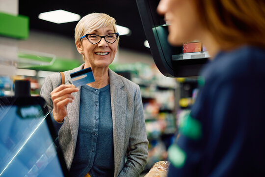 Happy senior woman paying with credit card at supermarket.