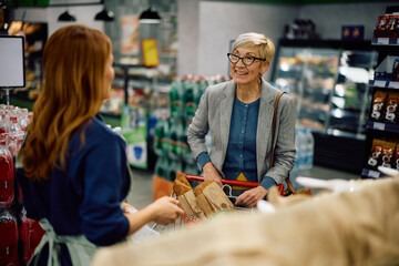 Happy senior woman talking to vendor at grocery store.