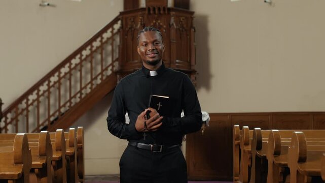 Young priest holding bible smiling in church