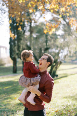 Fototapeta premium Laughing dad holding in his arms a laughing little girl in the park