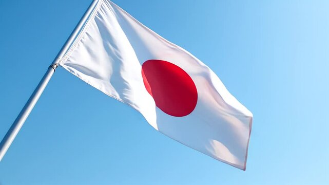 A vibrant image of the Japanese flag, featuring a bold red circle on a white background, billowing majestically in the breeze against a clear, cerulean blue sky
