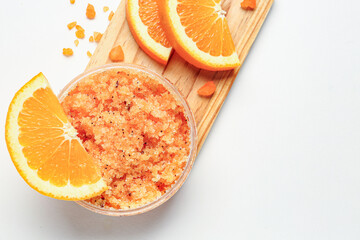 Wooden board with jar of natural body scrub and orange slices on light background, closeup