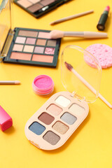 Decorative cosmetics with makeup brushes on yellow background, closeup