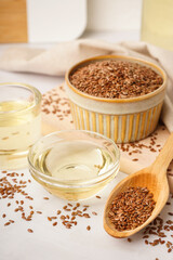 Bowl, glass with flax oil and spoon of seeds on white background