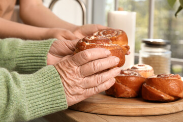 Senior woman with her granddaughter and tasty buns in kitchen, closeup