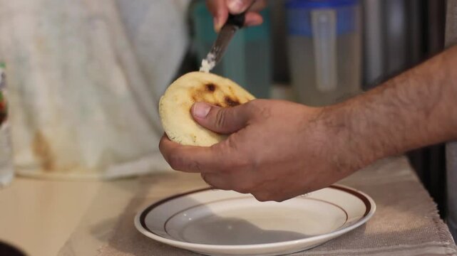 Opening the corn cake or arepa with a knife to fill it.