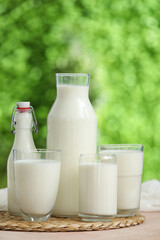 Glasses and bottles of fresh milk on beige table outdoors