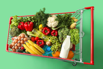 Shopping cart full of different food on green background
