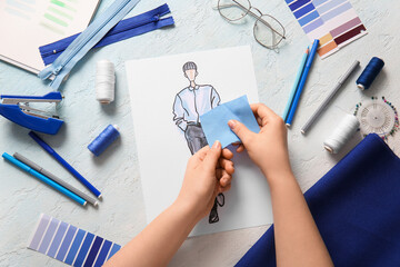 Female fashion designer holding piece of fabric, sketch and sewing supplies on light grunge...