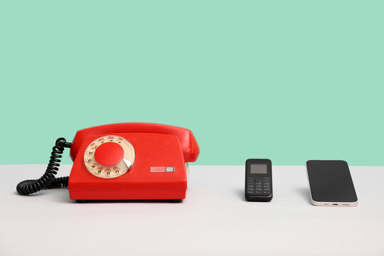 Retro telephone with button phone and smartphone on table against turquoise background. Concept of evolution