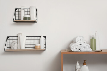 Folded towels and cosmetic products on shelves near white wall in bathroom