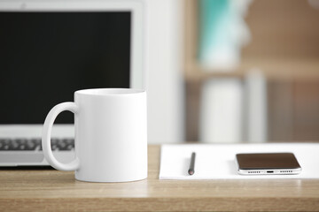 White ceramic mug on table near laptop and mobile phone in office