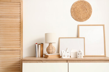 House shaped candle holders, books and lamp on chest of drawers near white wall in interior of living room