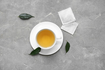Cup of hot green tea and leaves on grey background