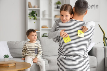 Little daughter attaching paper sheets with text KICK ME to her father's back at home. April fool's...