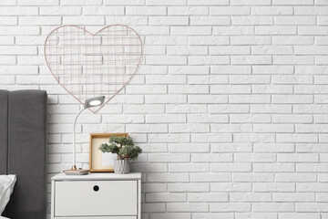 Glowing lamp on table near bed in light room