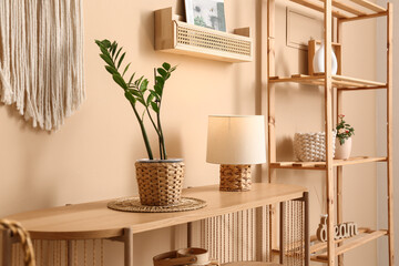 Wooden table with lamp and houseplant near beige wall in room