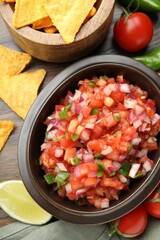 Delicious salsa in bowl, nacho chips and ingredients on wooden table, flat lay