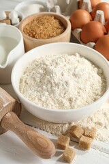 Rolling pin and ingredients for dough on white wooden table, closeup
