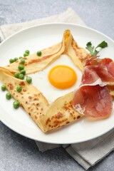 Delicious crepe with egg, bacon, arugula and green peas on grey table, closeup