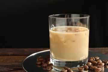 Coffee cream liqueur in glass and beans on wooden table, closeup. Space for text