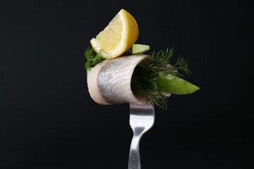 Fork with marinated herring fillet, cucumber, dill and lemon on black background, closeup