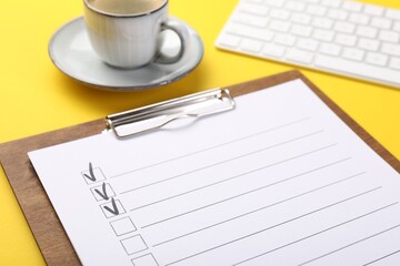 Checklist, coffee and keyboard on yellow background, closeup
