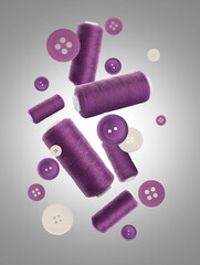 Many purple sewing threads and buttons falling on grey gradient background