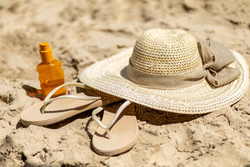 Summer beach accessories on warm sand featuring a straw hat, sandals, and sunscreen for a relaxing...