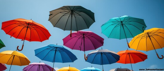 Obraz premium Colorful umbrellas float against a clear blue sky