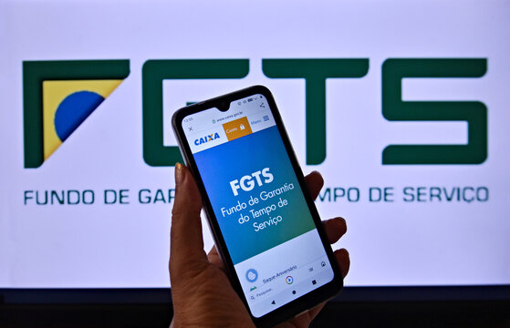The FGTS logo on a cell phone screen being held by a hand. In the background, the Brazilian FGTS logo. Rio de Janeiro, Brazil - 04.11.2025.