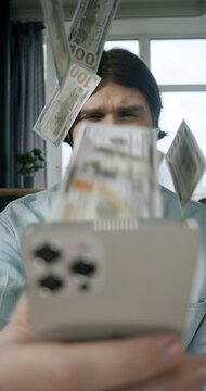 The man make money online with smartphone.  Money rain flow through the smartphone. Dollar bills flying, floating in investor face. Cash flow. Online winning. Business making easy money online concept