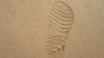 Shoe print on smooth beach sand, highlighting texture and detail. A single footprint symbolizes travel, exploration, and solitude, blending natural patterns with human presence.